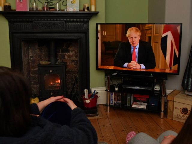 Members of a family listen as Britain's Prime Minister Boris Johnson makes a televised address to the nation from inside 10 Downing Street in London, with the latest instructions to stay at home to help contain the Covid-19 pandemic, from a house in Liverpool, north west England on March 23, …