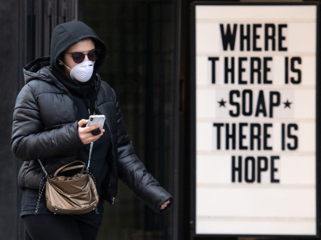 LONDON, ENGLAND - MARCH 17: A woman wearing a protective mask walks past a sign in a cosmetic shop window on March 17, 2020 in London, England. Boris Johnson held the first of his public daily briefing on the Coronavirus outbreak yesterday and told the public to avoid theatres, going …