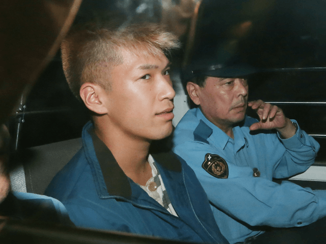 Murder suspect Satoshi Uematsu (L) sits in the back seat of a police vehicle as he returns