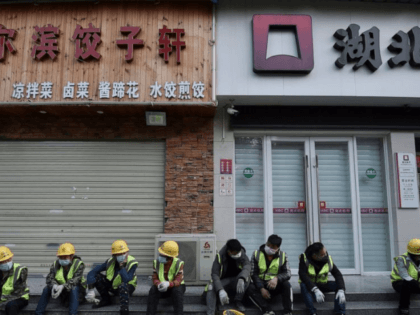 In this Sunday, Feb. 23, 2020, photo, workers take a rest near the closed restaurant and bank in Wuhan in central China's Hubei province. Warning that China's virus epidemic is "still grim and complex," President Xi Jinping called Sunday for more efforts to stop the outbreak, revive industry and prevent …