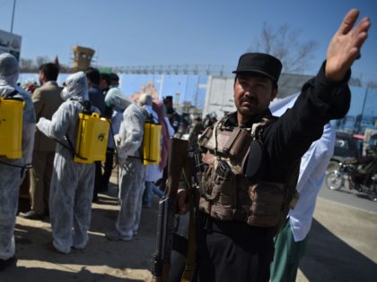 An Afghan policeman gestures as volunteers wearing a hazmat suits and a facemasks gather o