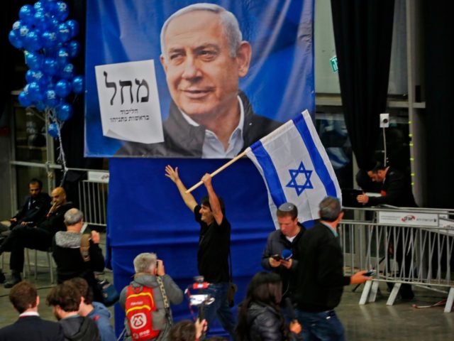A man reacts as he holds up an Israeli flag while standing behind a giant Likud party elec