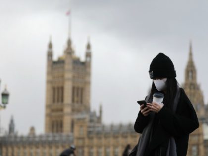 A pedestrian wearing a face mask walks along Westminster Bridge in front of the Houses of Parliament in London on March 12, 2020. - The British government was expected Thursday to implement the second phase of its plan to deal with the coronavirus outbreak but rejected calls for parliament to …