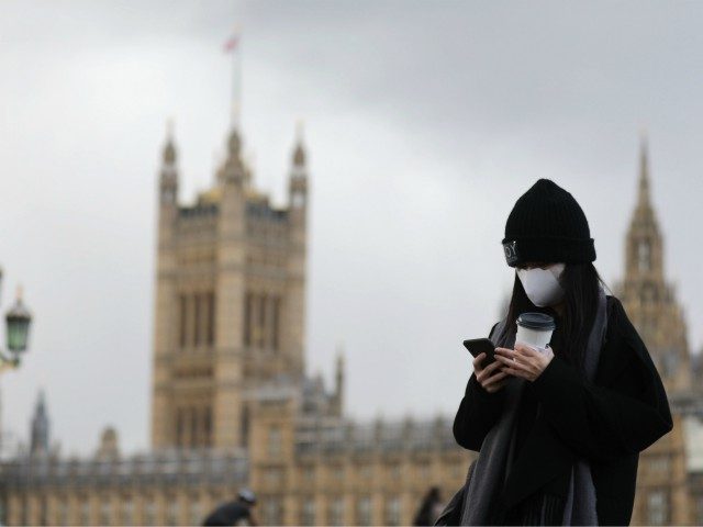 A pedestrian wearing a face mask walks along Westminster Bridge in front of the Houses of