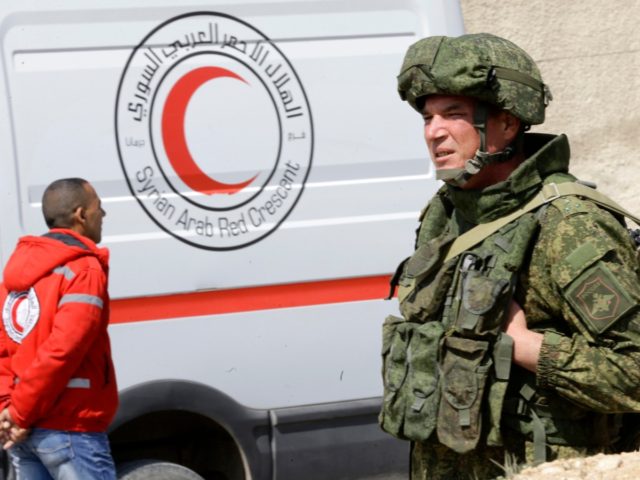 A Russian military police officer stands before a Syrian Red Crescent ambulance on the gov