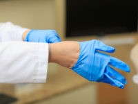 Doctor dress gloves on hands on the background of the operation room. Real nurse putting on sterile gloves. Working in medical clinic with sterile gloves. Medical protocol for employees of nursing.