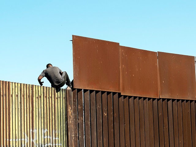 TOPSHOT - A man crosses over the US/Mexico border fence from Mexicali to Calexico, at Mexi