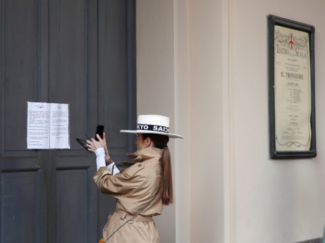 A woman takes a picture of a notice on the entrance doors, written in Italian and English,