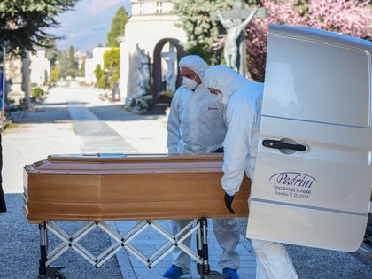Undertakers wearing a face mask and overalls unload a coffin out of a hearse on March 16,