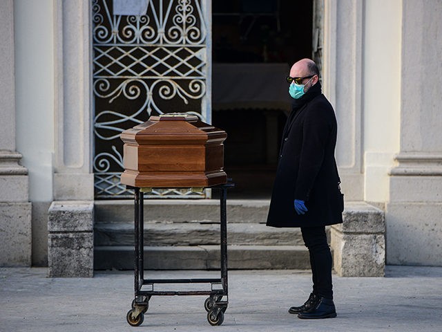 A man stands by the coffin of his mother during a funeral service in the closed cemetery o