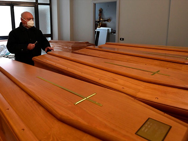 Italian priest of the small town of Albino, Don Giuseppe Locattelli, wearing a face mask, blesses coffins of the deceased in a mortuary cell on March 25, 2020 in Albino, during the country's lockdown following the COVID-19 new coronavirus pandemic. (Photo by MIGUEL MEDINA / AFP) (Photo by MIGUEL MEDINA/AFP …