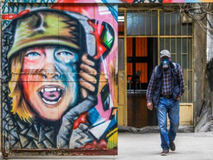 A Lebanese man, wearing facial gas mask as part of health safety measures related to the spread of COVID-19, walks past a graffiti in the northern port city of Tripoli, on March 16, 2020 - Lebanon, on March 15, urged people to stay at home for two weeks and prepared …