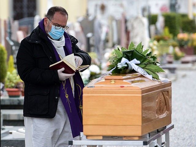 A priest wearing a face mask checks a book of funeral rites as he gives the last blessing to a deceased person, by a coffin during a funeral ceremony outside the cemetery of Bolgare, Lombardy, on March 23, 2020 during the COVID-19 new coronavirus pandemic. (Photo by Piero CRUCIATTI / …
