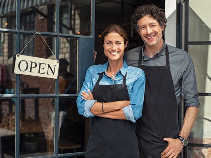 Two cheerful small business owners smiling and looking at camera while standing at entranc
