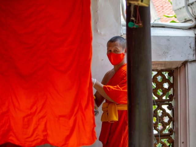 A Buddhist monk stands with a food container at Wat Arun Buddhist temple in Bangkok, Thail