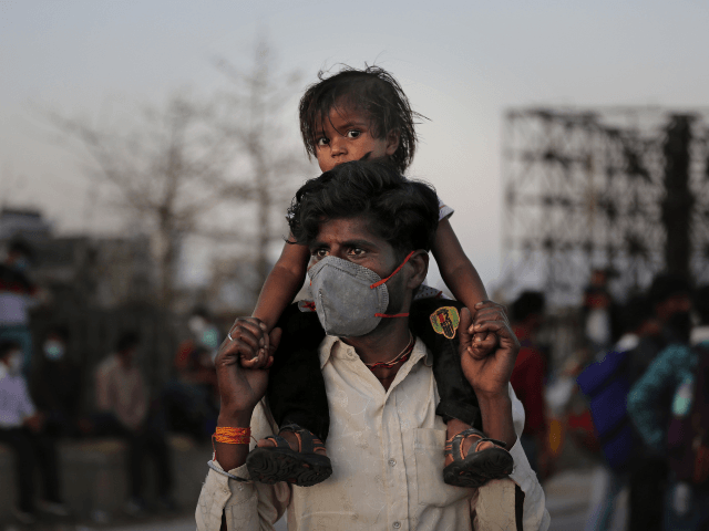 An Indian migrant worker carries a child on his shoulders as they wait for transportation