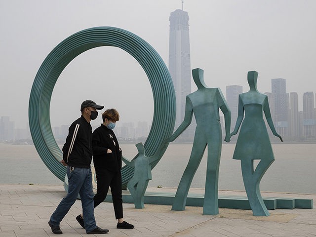 Residents wearing masks against the coronavirus walk past sculpture along the banks of the