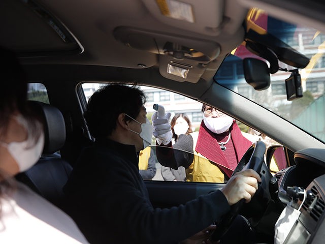 A man wearing a face mask has his temperature checked upon her arrival for a Sunday drive-