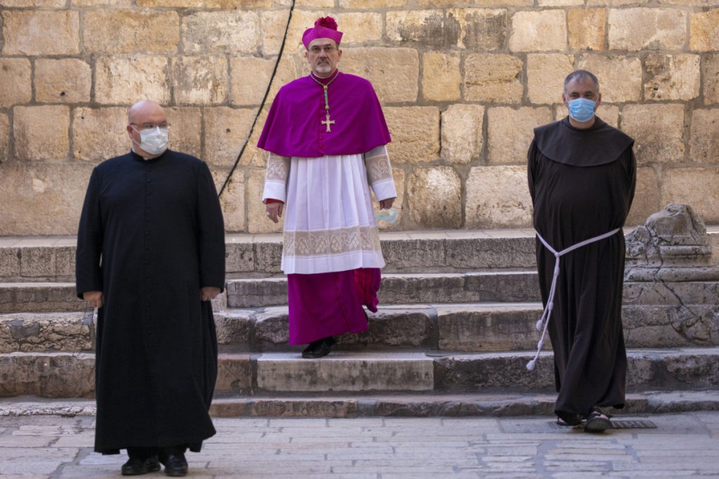 Archbishop Pierbattista Pizzaballa, center, arrives at the Church of the Holy Sepulchre, a place where Christians believe Jesus Christ was buried, during a lockdown following government measures to help stop the spread of the new coronavirus, during Holy Thursday in Jerusalem's old city, Thursday, April 9, 2020. The traditional Holy Thursday procession is taking place inside the church without public attendance this year due to restrictions imposed to contain the spread of the coronavirus. (AP Photo/Ariel Schalit)