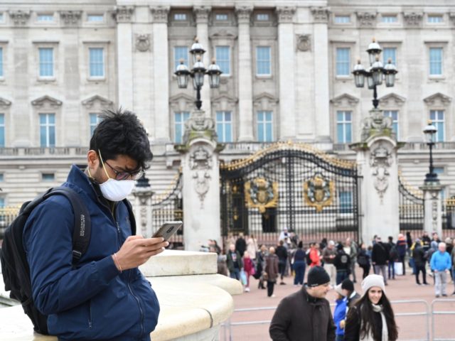 A tourist wearing a mask checks his cellphone in front of Buckingham Palace in London on March 14, 2020. - British Prime Minister Boris Johnson, who has faced criticism for his country's light touch approach to tackling the coronavirus outbreak, is preparing to review its approach and ban mass gatherings, …