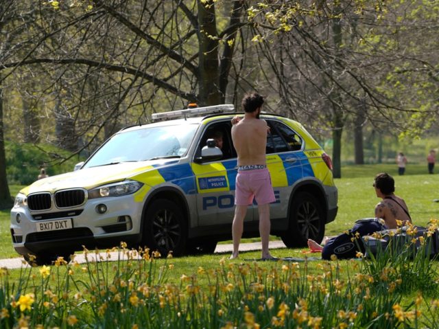 Police officers sit in a car as they talk with two men who had been sunbathing in St James