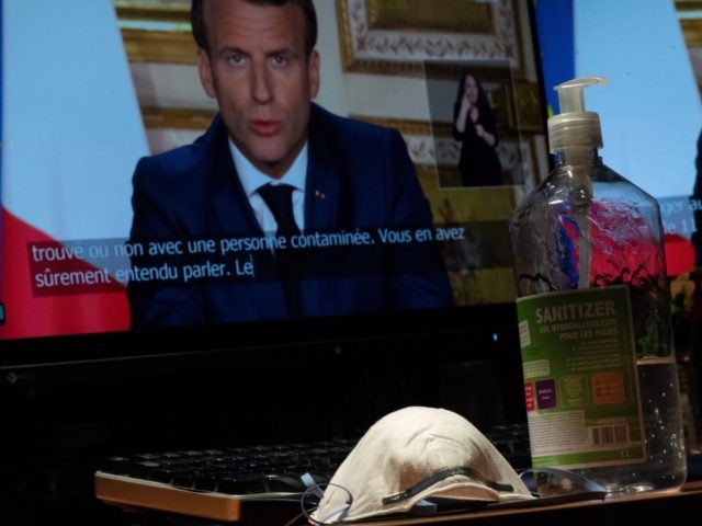 French President Emmanuel Macron is seen on a monitor in Paris, next to a face mask and a bottle of hand sanitiser, as he speaks from the Elysee Palace during a televised address to the nation on April 13, 2020, on the 28th day of a lockdown in France aimed …