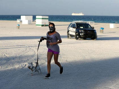 A jogger and her dog are turned away from a closed beach by a police officer, Wednesday, March 25, 2020, in Miami Beach, Fla.'s famed South Beach. (AP Photo/Wilfredo Lee)