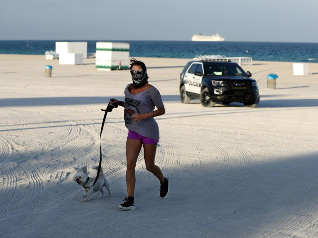 A jogger and her dog are turned away from a closed beach by a police officer, Wednesday, M