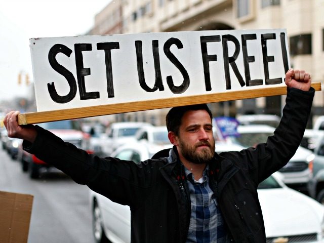 Steve Polet holds a sign during a protest at the State Capitol in Lansing, Mich., Wednesday, April 15, 2020. Flag-waving, honking protesters drove past the Michigan Capitol on Wednesday to show their displeasure with Michigan Gov. Gretchen Whitmer's orders to keep people at home and businesses locked during the new …