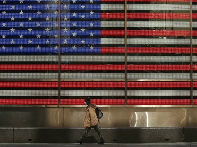 NEW YORK, NEW YORK - APRIL 25: A pedestrian, wearing a protective face mask walks past the American flag video board in Times Square during the coronavirus pandemic on April 25, 2020 in New York City. COVID-19 has spread to most countries around the world, claiming over 200,000 lives with …