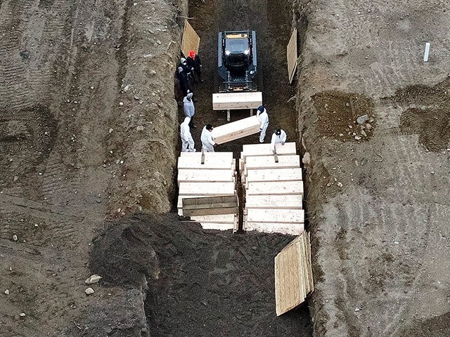 Workers wearing personal protective equipment bury bodies in a trench on Hart Island, Thur