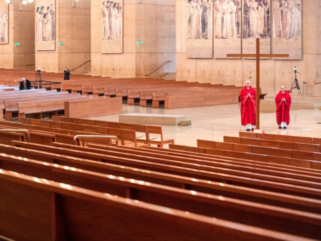 Archbishop Jose Gomez (L) stands before a cross during Good Friday service with Father Brian Nunez (R) inside the nearly empty Cathedral of Our Lady of the Angels on April 10, 2020 in Los Angeles. - Service was held on video without parishioners. The global coronavirus death toll topped 100,000 …