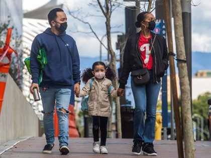 A family walks wearing masks in Downtown Los Angeles on March 22, 2020, during the coronavirus (COVID-19) outbreak. - The US president on March 22 said he had ordered the deployment of emergency medical stations with capacity of 4,000 hospital beds to coronavirus hotspots around the United States. (Photo by …