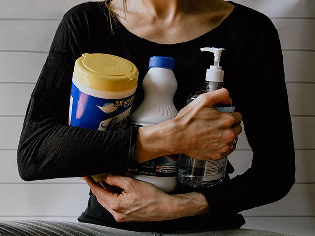 Woman holding disinfectant products such as Lysol, Clorox, and Purell.