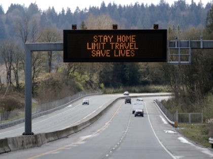 A sign overhead on an unusually quiet highway reminds drivers to "Stay home, limit travel,