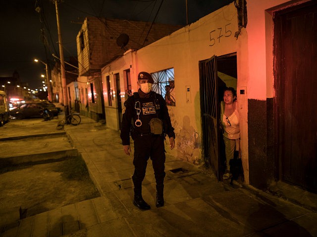 In this April 8, 2020 photo, a neighbor watches a police operation to ensure the curfew declared by the government due to the new coronavirus pandemic, in El Callao, on the outskirts of Lima, Peru. Business has fallen for funeral homes that specialize in selling coffins for victims of violent …