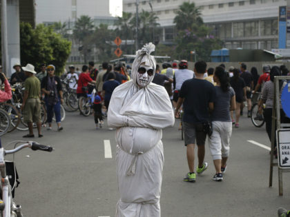 A man dressed as a shrouded ghost locally known as a "pocong" busks for small money during a car free day in the main business district in Jakarta, Indonesia, Sunday, July 17, 2016. (AP Photo/Dita Alangkara)