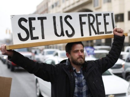 In this April 15, 2020, photo, Steve Polet holds a sign during a protest at the State Capi