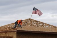 The American flag flutters in the wind as work is done on the roof of a building under construction in Sacramento, Calif., Tuesday, March 31, 2020. While most Californian's have spent more than a week under a mandatory stay-at-home order, because of the coronavirus, construction work is among the jobs …