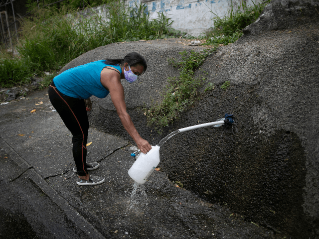 A woman wearing a face mask as a precaution amid the spread of the new coronavirus collects water from a mountainside on the side of the road to take home in Caracas, Venezuela, on International Earth Day, Wednesday, April 22, 2020. Many people in Venezuela don't have running water in …