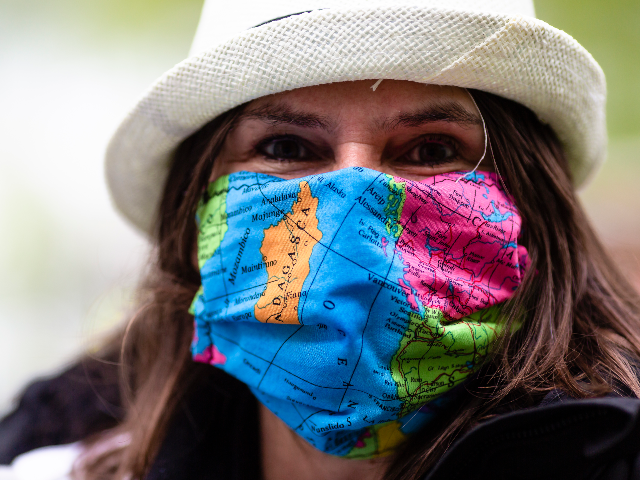 A woman wears a wears a face mask with a world map design as the attends a protest of trav