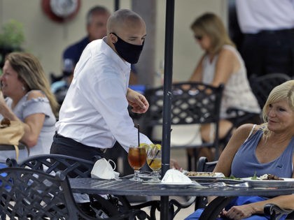 A foodserver at the Parkshore Grill restaurant wears a protective face mask as he waits on customers Monday, May 4, 2020, in St. Petersburg, Fla. Several restaurants are reopening with a 25% capacity as part of Florida Gov. Ron DeSantis' plan to stop the spread of the coronavirus. (AP Photo/Chris …