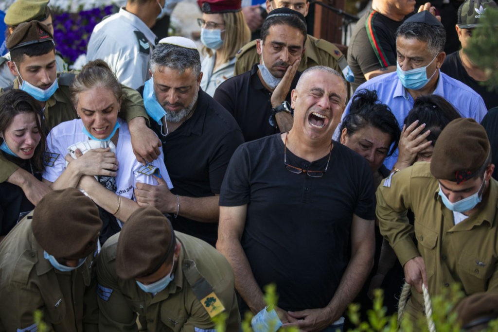 Baruch, right, and Nava, left, parents of Israeli army Staff Sgt. Amit Ben-Yigal grieve during his funeral as soldiers and family wear face masks to protect against the spread of the coronavirus in Beer Yaakov, Israel, Tuesday, May 12, 2020. Ben Ygal, 21, was killed early Tuesday during a West Bank arrest raid when a rock thrown off a rooftop struck him in the head, the military said, capping a surge in violence ahead of a visit to the region by the U.S. secretary of state. (AP Photo/Ariel Schalit)