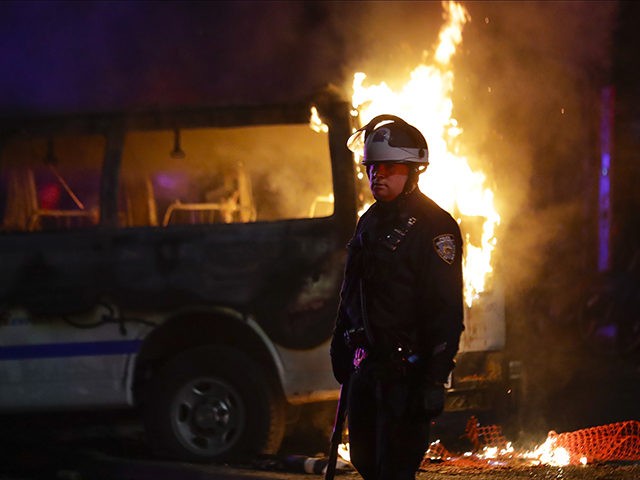A police officer walks past a burning police vehicle on DeKalb Avenue in the Brooklyn borough of New York, Friday, May 29, 2020, after protesters gathered at Barclays Center to express anger over the death of George Floyd, a black man who died Memorial Day while in police custody in …