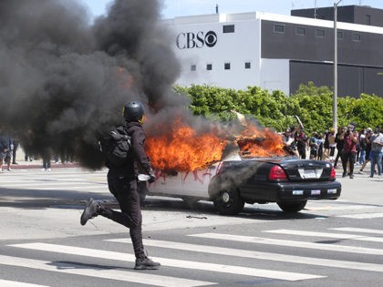 A person runs while a police vehicle is burning during a protest over the death of George