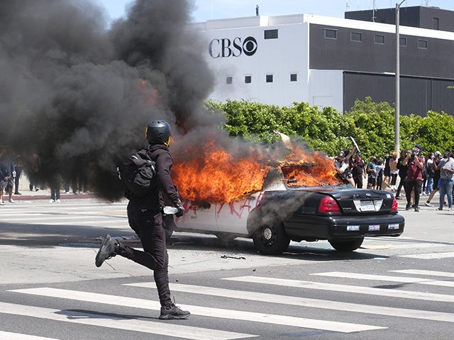 A person runs while a police vehicle is burning during a protest over the death of George Floyd in Los Angeles, Saturday, May 30, 2020. Protests across the country have escalated over the death of George Floyd who died after being restrained by Minneapolis police officers on Memorial Day, May …