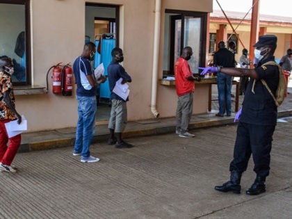 An Ugandan security officer asks for social distancing as truck drivers wait in a line to go through the Uganda's immigration office in Malaba, a city bordering with Kenya, in Uganda, on April 29, 2020. - All truck drivers ferrying goods crossing the border from Kenya must take a test …