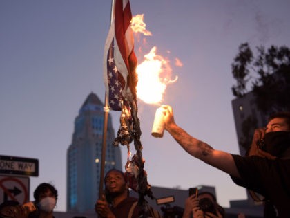 A man burns an upsidedown US flag as protesters gather in downtown Los Angeles on May 27,