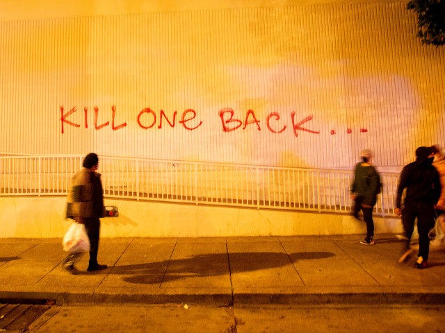 People walk past graffiti as protesters face off against police during a demonstration over the death of George Floyd, a black man who died after a white policeman kneeled on his neck for several minutes, in Oakland California, on May 29, 2020. - Protesters shouted and threw objects at police …