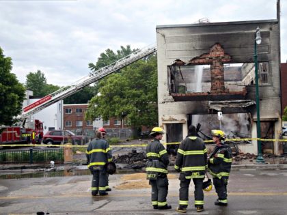 Firefighters stand as an aerial hose sends water on hot spots of a building destroyed near